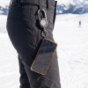 Telefoon hangt aan een uitrolbaar koord aan een zwarte skibroek op een besneeuwde piste